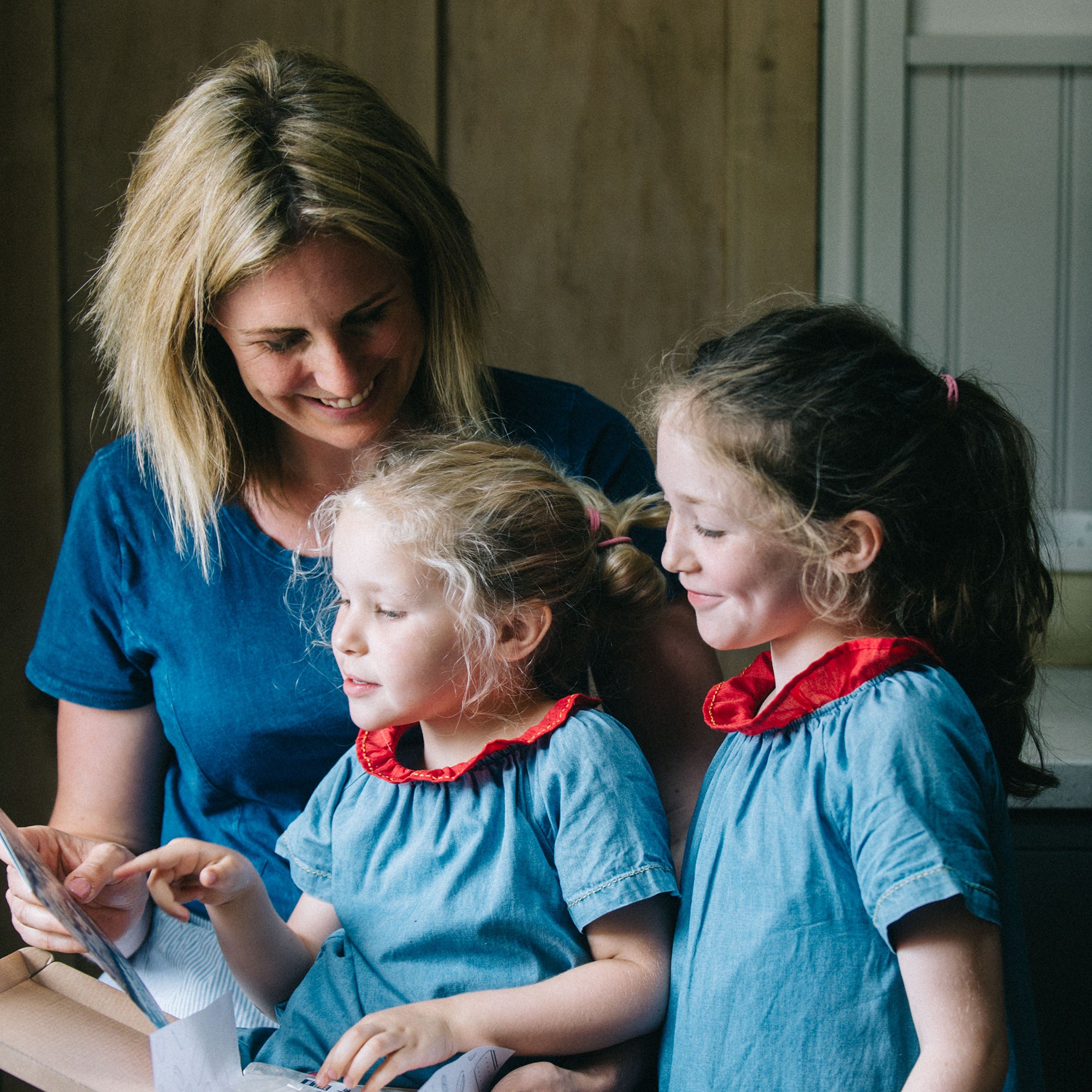 Woman and two young girls in matching outfits looking at a tablet together.
